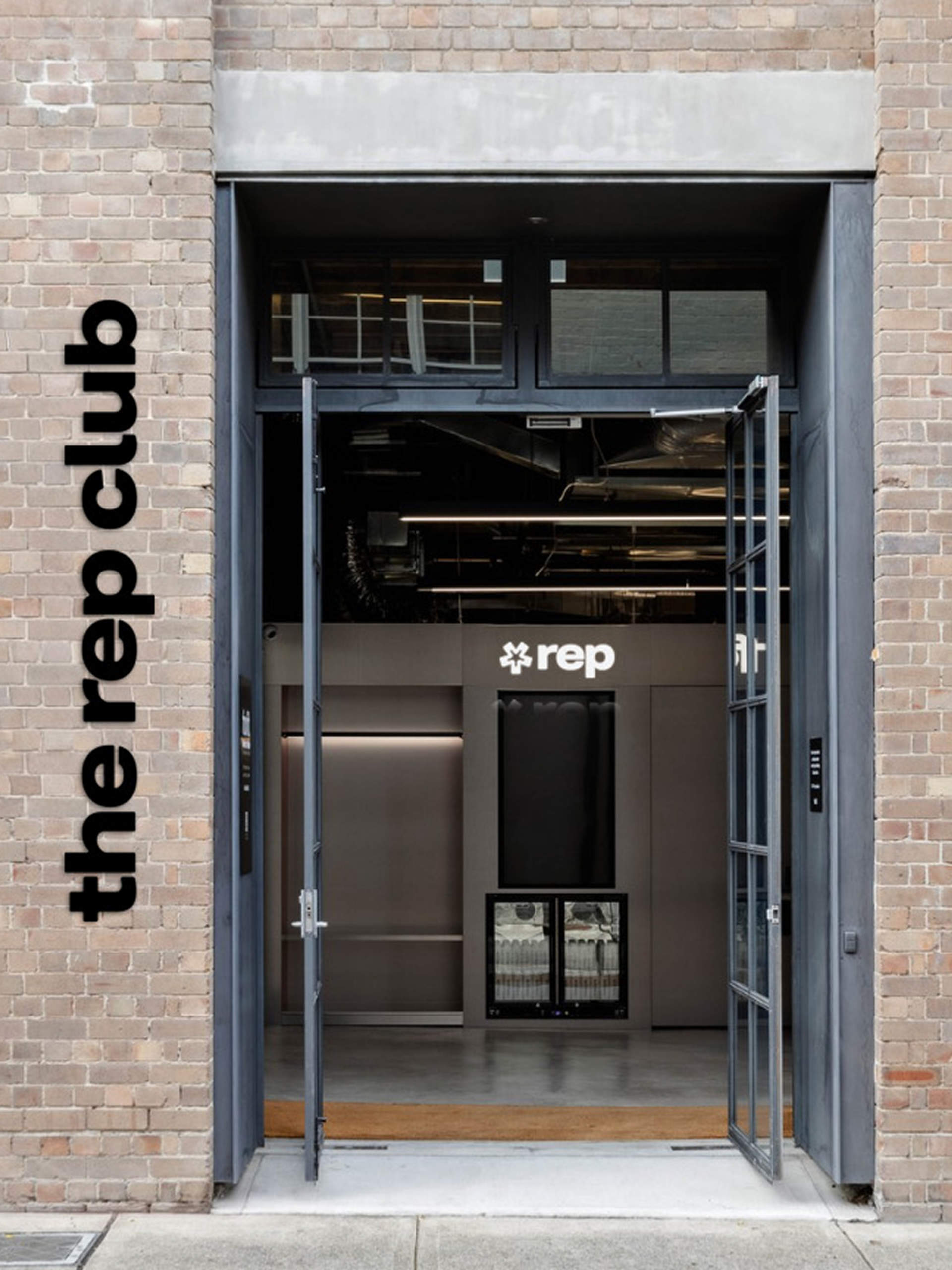 The Rep Club's brand wordmark applied vertically to the brick exterior of the Redfern Sydney studio entrance, with the "rep" combo mark logo visible on the interior reception wall, showing real-world brand identity application designed by Christie Evenson Design Studio